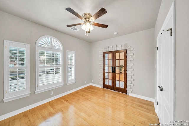 empty room with visible vents, a ceiling fan, baseboards, french doors, and light wood-type flooring