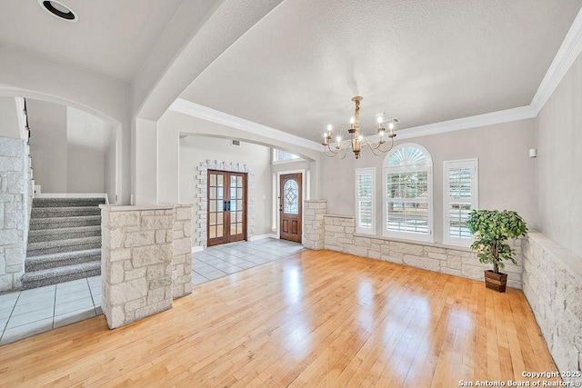 foyer featuring stairs, light wood finished floors, an inviting chandelier, and crown molding