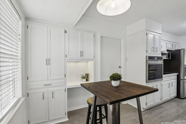 kitchen with a textured ceiling, light tile patterned flooring, white cabinetry, light countertops, and appliances with stainless steel finishes