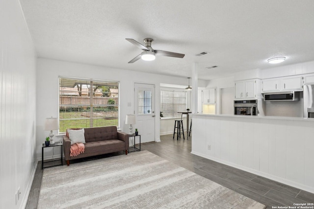 living area with wood tiled floor, visible vents, ceiling fan, and a textured ceiling