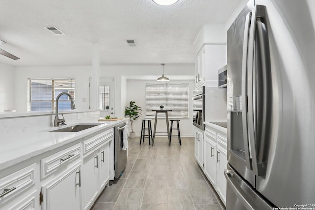 kitchen featuring visible vents, white cabinets, decorative light fixtures, stainless steel appliances, and a sink