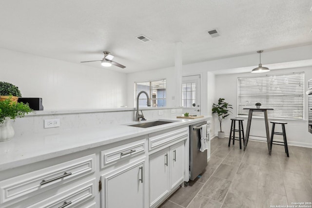 kitchen featuring a sink, white cabinetry, hanging light fixtures, stainless steel dishwasher, and light countertops