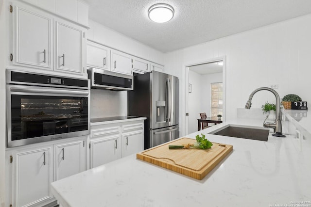 kitchen featuring white cabinets, a textured ceiling, stainless steel appliances, and a sink