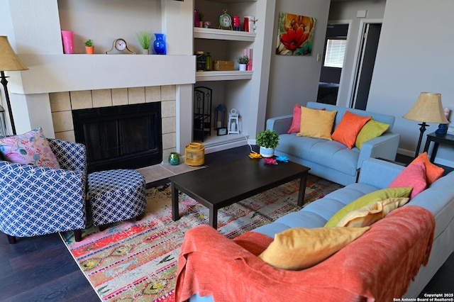 living room with built in shelves, dark wood finished floors, and a tile fireplace