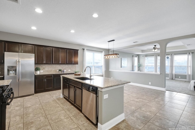 kitchen featuring an island with sink, open floor plan, stainless steel appliances, dark brown cabinets, and a sink