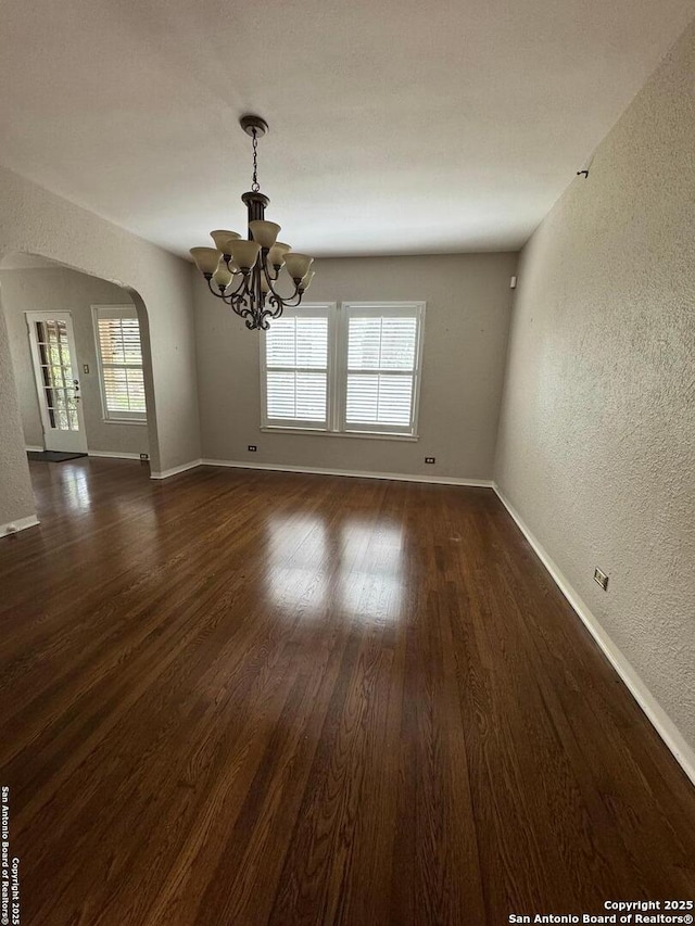 unfurnished dining area with a chandelier, a textured wall, baseboards, and plenty of natural light