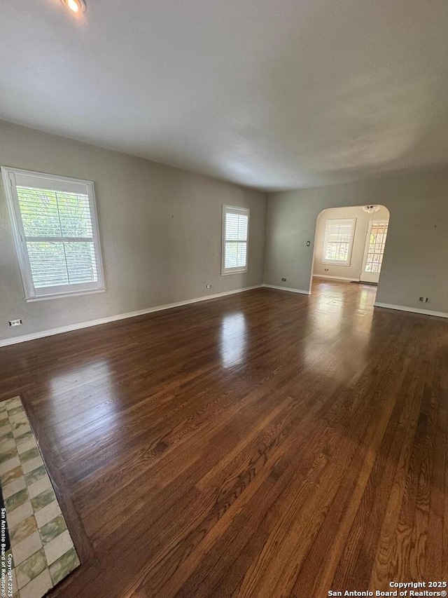 unfurnished room featuring baseboards, wood finished floors, and arched walkways