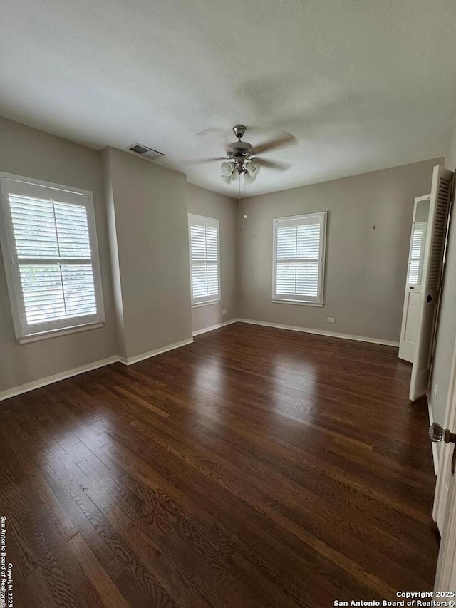 empty room featuring baseboards, a ceiling fan, visible vents, and dark wood finished floors