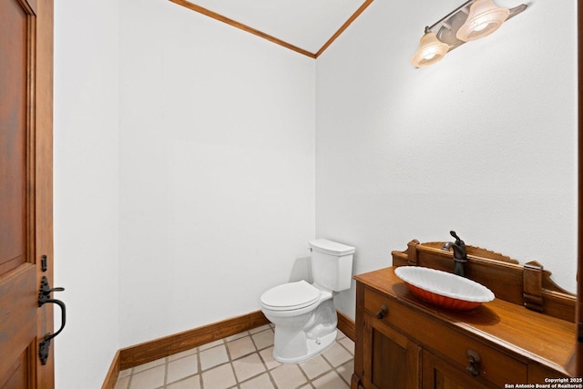 half bathroom featuring baseboards, crown molding, vanity, and toilet