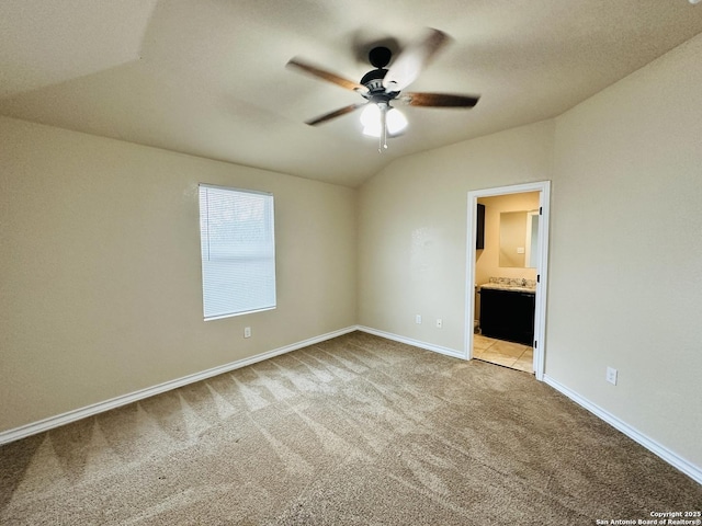 unfurnished bedroom featuring lofted ceiling, light carpet, connected bathroom, ceiling fan, and baseboards