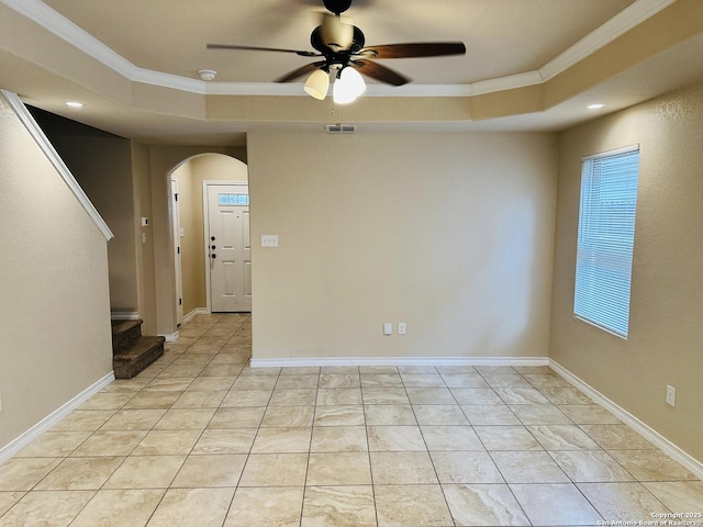 empty room featuring arched walkways, a tray ceiling, visible vents, and crown molding