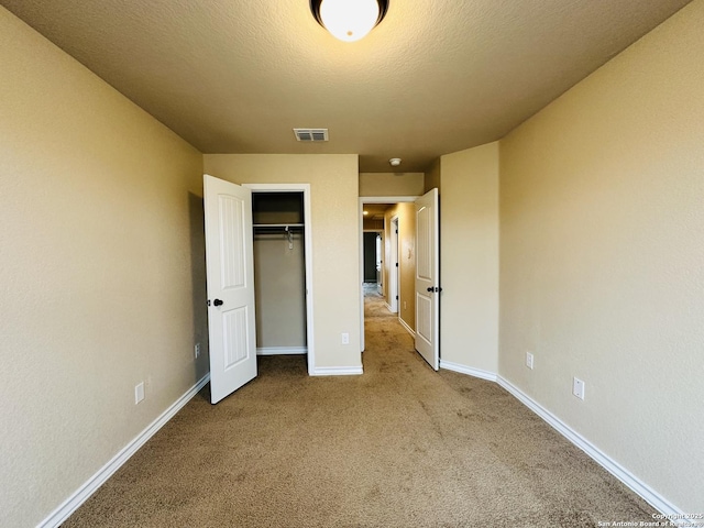 unfurnished bedroom featuring a closet, light colored carpet, visible vents, a textured ceiling, and baseboards