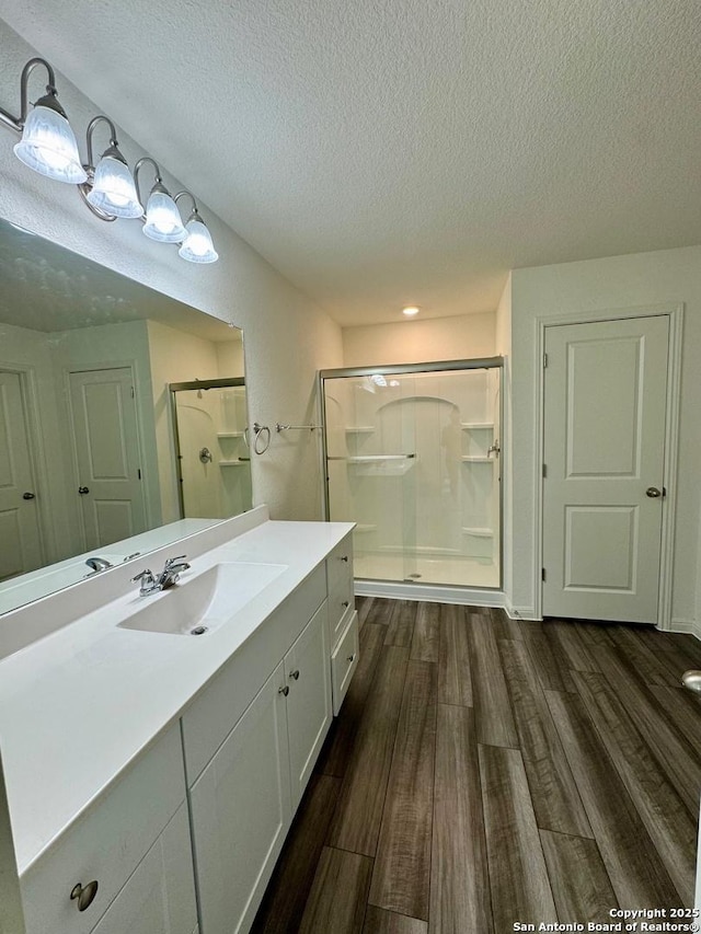 bathroom with a textured ceiling, a shower stall, vanity, and wood finished floors