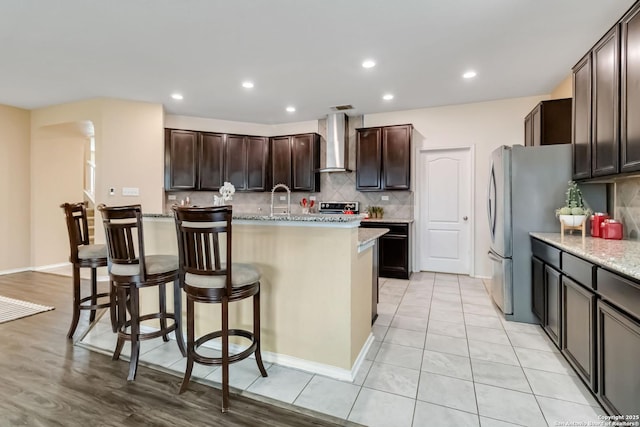 kitchen with wall chimney exhaust hood, light stone counters, a kitchen bar, and a center island with sink