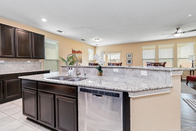 kitchen with a center island with sink, decorative backsplash, stainless steel dishwasher, dark brown cabinetry, and a sink