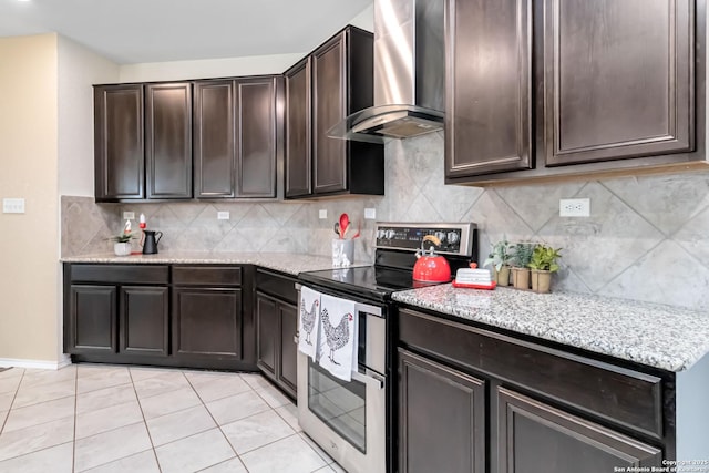 kitchen with light stone counters, dark brown cabinetry, double oven range, decorative backsplash, and wall chimney exhaust hood