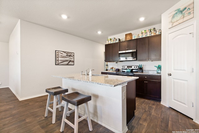 kitchen with a breakfast bar, a sink, dark brown cabinets, appliances with stainless steel finishes, and a center island with sink