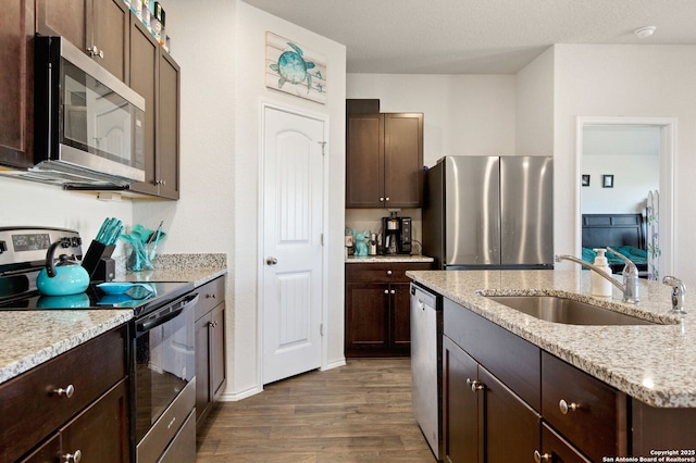 kitchen with dark brown cabinetry, dark wood-style floors, appliances with stainless steel finishes, light stone counters, and a sink