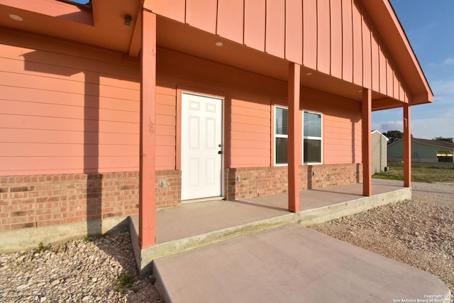 view of exterior entry with stone siding, board and batten siding, and a patio area