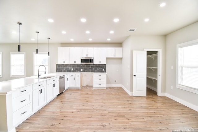 kitchen with a sink, stainless steel appliances, light countertops, and pendant lighting