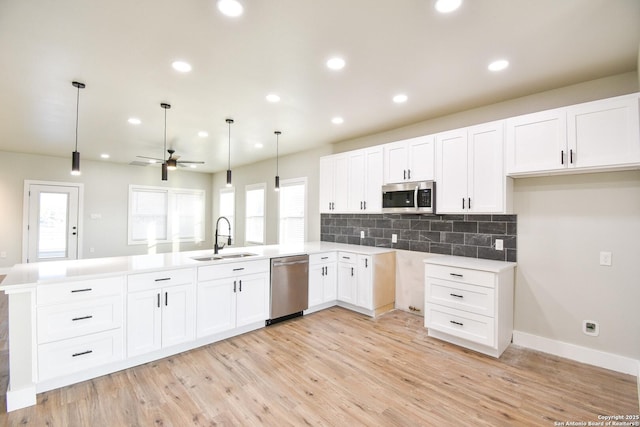 kitchen featuring decorative light fixtures, a peninsula, stainless steel appliances, light countertops, and a sink