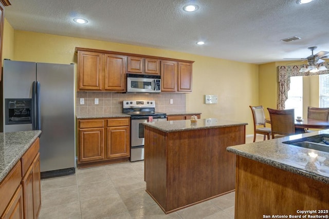 kitchen with visible vents, brown cabinetry, decorative backsplash, appliances with stainless steel finishes, and a center island