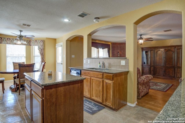 kitchen featuring stainless steel dishwasher, visible vents, a kitchen island, and a sink