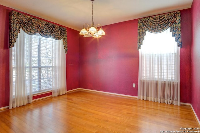 unfurnished room with baseboards, a chandelier, and wood finished floors