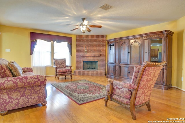 living room featuring a textured ceiling, light wood-style flooring, a fireplace, and visible vents