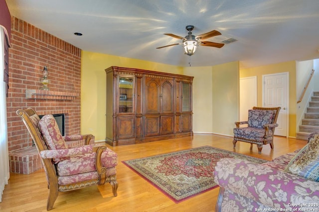 living area with visible vents, ceiling fan, light wood-style flooring, stairs, and a fireplace