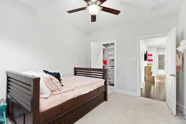 bedroom featuring light carpet, baseboards, visible vents, a ceiling fan, and a walk in closet