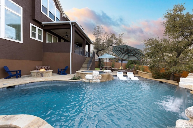 pool at dusk with ceiling fan, an outdoor fire pit, fence, stairs, and a patio area