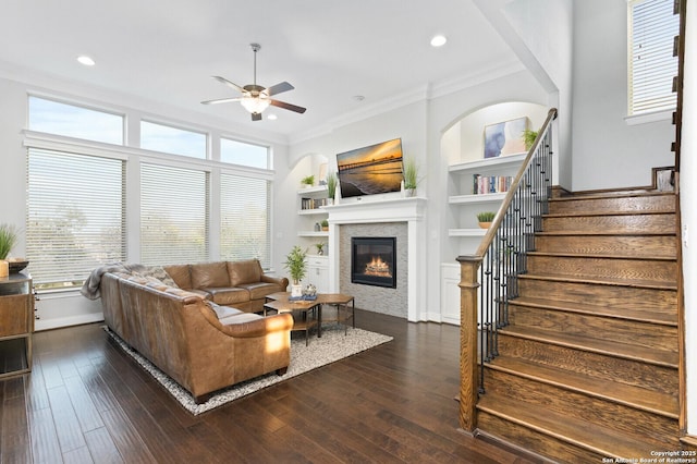 living room with built in shelves, crown molding, dark wood finished floors, and stairs