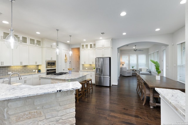 kitchen featuring stainless steel appliances, arched walkways, white cabinets, and dark wood finished floors