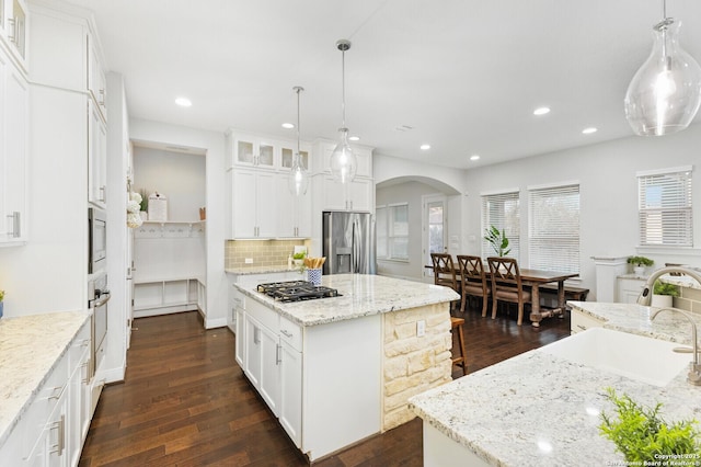 kitchen with arched walkways, stainless steel appliances, dark wood-style flooring, a sink, and a kitchen island