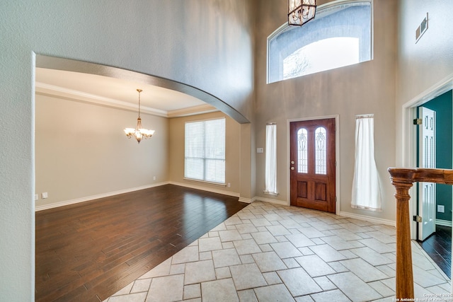 entryway with crown molding, plenty of natural light, light wood-type flooring, and a notable chandelier