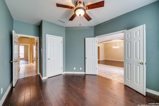 unfurnished bedroom with arched walkways, dark wood-style flooring, visible vents, and baseboards