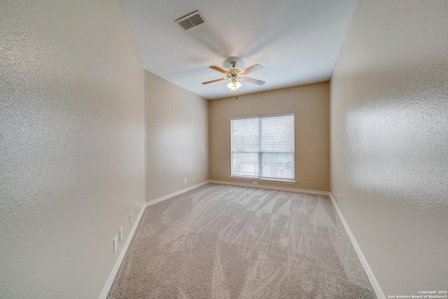 unfurnished room with a textured wall, light colored carpet, a ceiling fan, visible vents, and baseboards