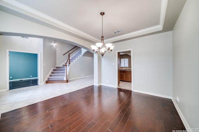 empty room featuring a tray ceiling, visible vents, arched walkways, and wood finished floors