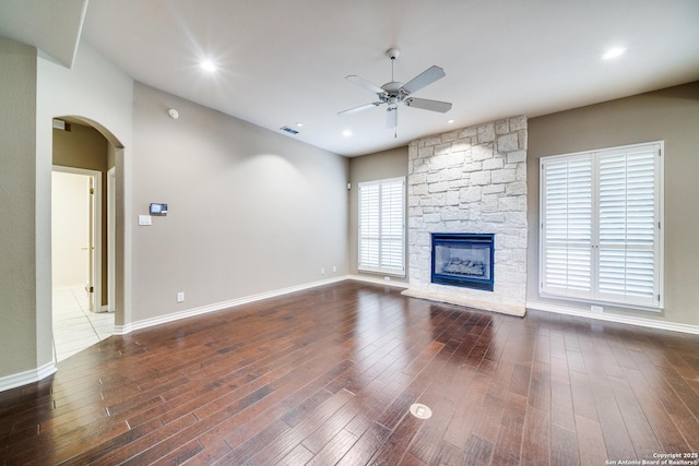 unfurnished living room featuring visible vents, dark wood finished floors, arched walkways, ceiling fan, and a fireplace