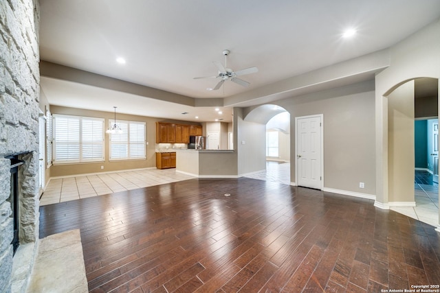 unfurnished living room with light wood-style floors, ceiling fan, arched walkways, and a stone fireplace