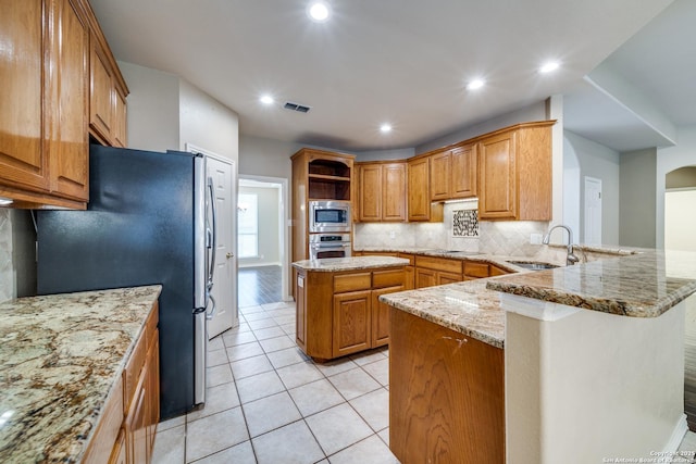 kitchen with appliances with stainless steel finishes, brown cabinets, a peninsula, light stone countertops, and a sink