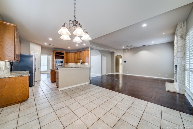 kitchen featuring brown cabinetry, appliances with stainless steel finishes, open floor plan, a fireplace, and light tile patterned flooring