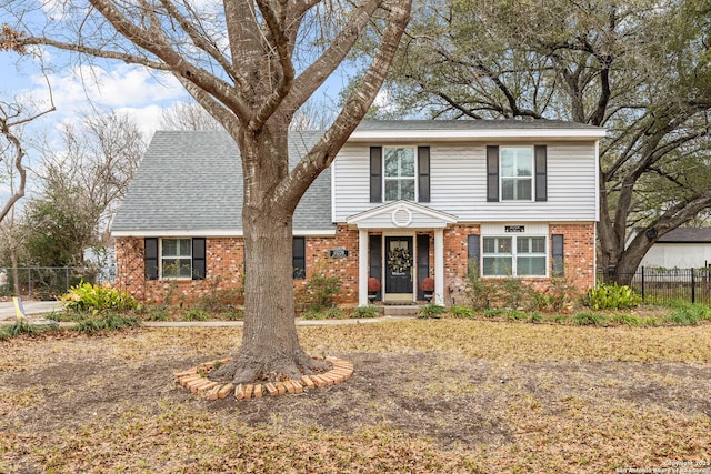 traditional-style house featuring a shingled roof, brick siding, and fence