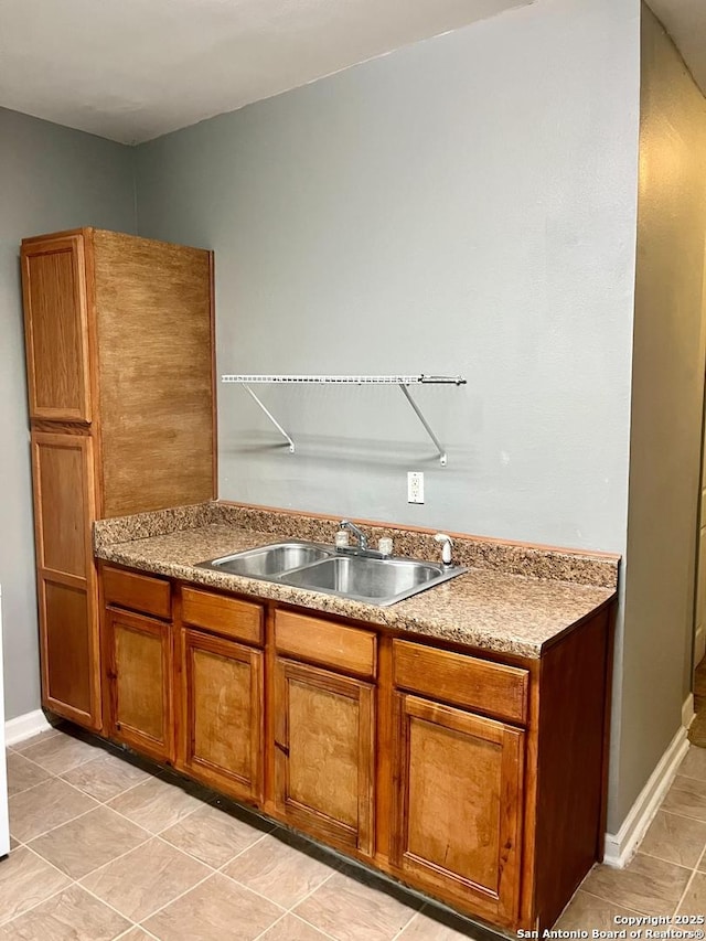 kitchen with baseboards, brown cabinets, light countertops, a sink, and light tile patterned flooring