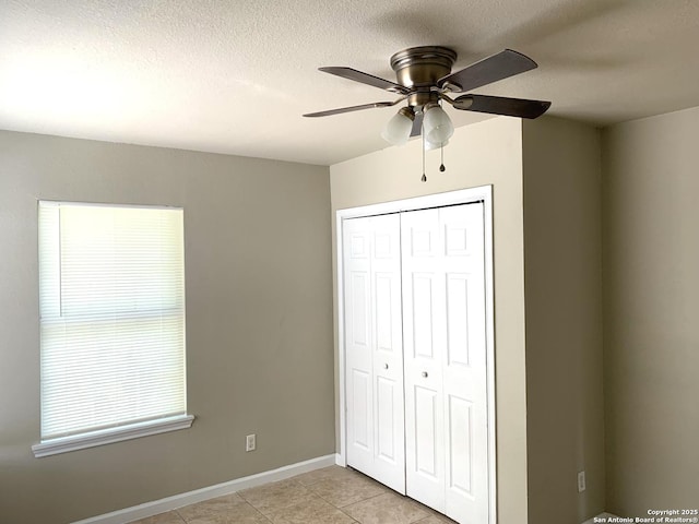 unfurnished bedroom with a textured ceiling, light tile patterned floors, a ceiling fan, baseboards, and a closet