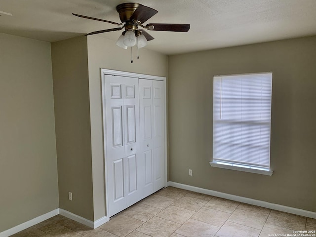 unfurnished bedroom featuring a ceiling fan, light tile patterned floors, baseboards, and a closet