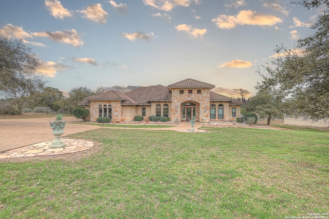 mediterranean / spanish home with stone siding, a lawn, a tiled roof, and stucco siding