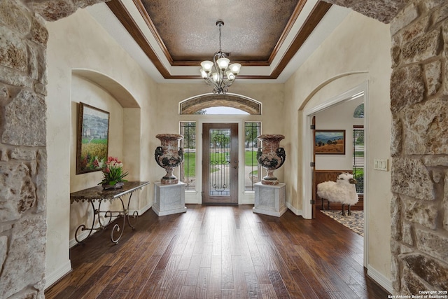 foyer entrance with baseboards, ornamental molding, wood-type flooring, a raised ceiling, and an inviting chandelier