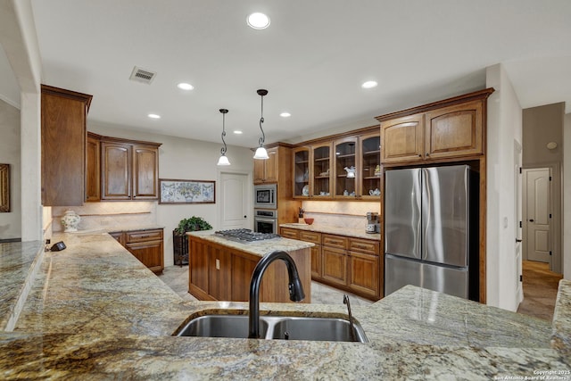 kitchen with light stone countertops, stainless steel appliances, a sink, visible vents, and brown cabinets